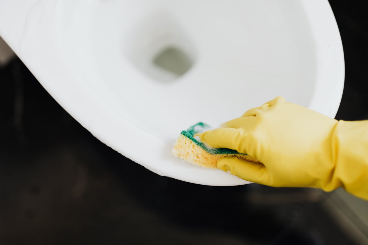 Close-up of a toilet being cleaned with a sponge and yellow gloves. Hygiene and sanitation concept.